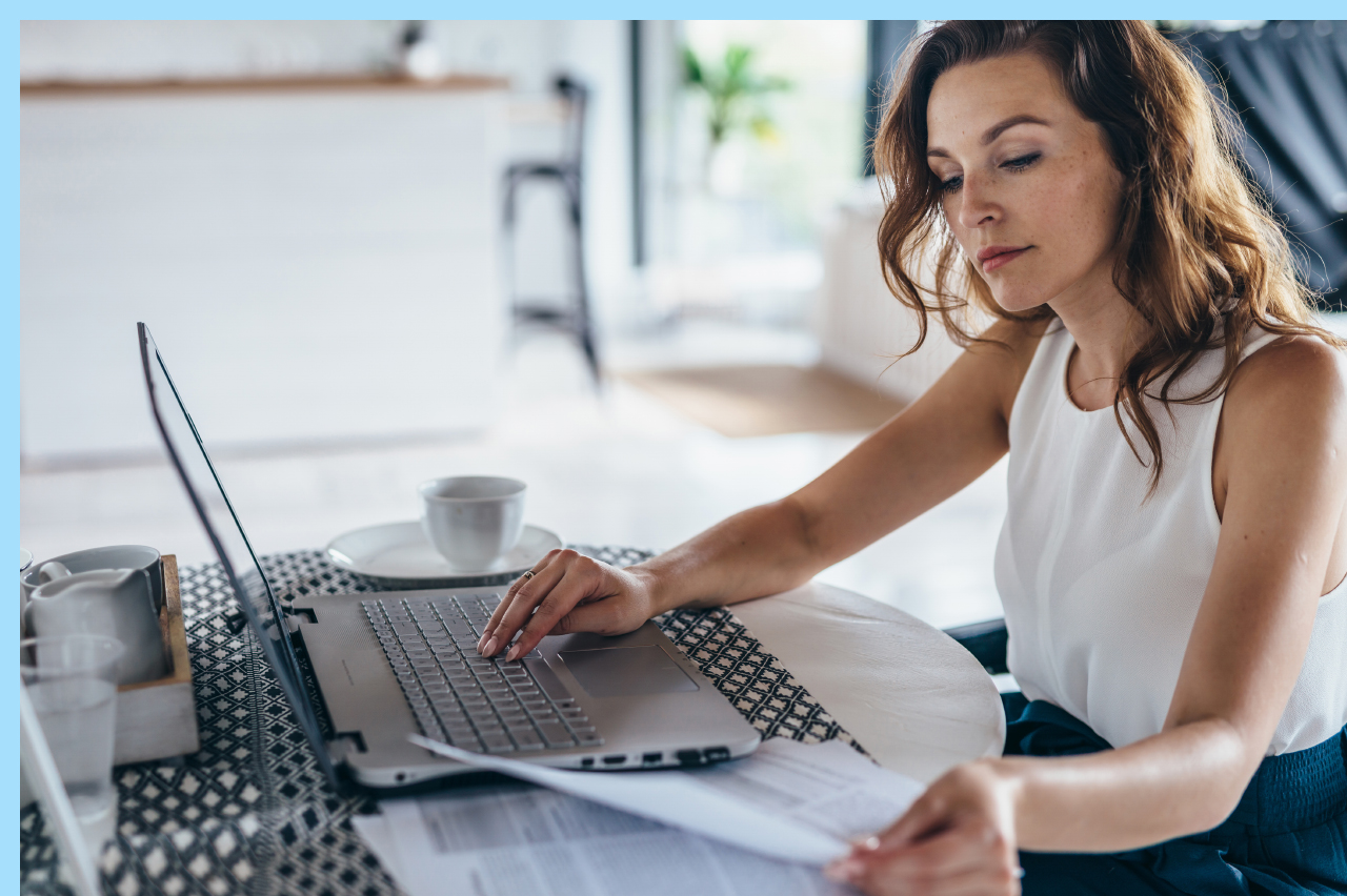 woman looking over paperwork while she works on her computer